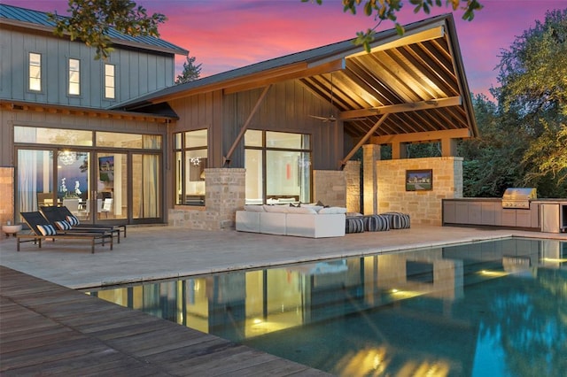 back of property featuring an outdoor living space, exterior kitchen, metal roof, stone siding, and a standing seam roof