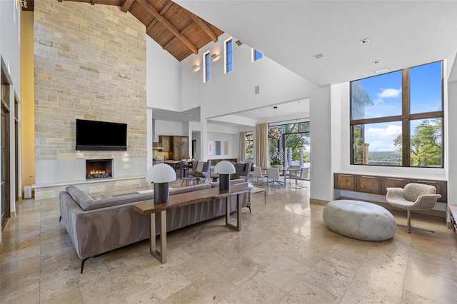 living room with beamed ceiling, high vaulted ceiling, stone tile flooring, a stone fireplace, and wood ceiling