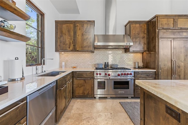 kitchen featuring a sink, tasteful backsplash, wall chimney range hood, light stone countertops, and high end appliances