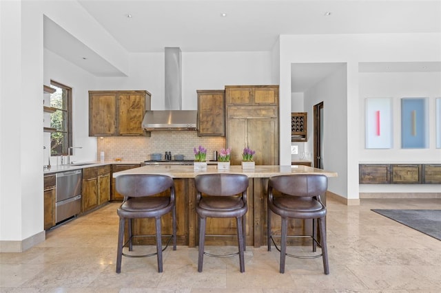 kitchen featuring a kitchen island, light countertops, wall chimney range hood, brown cabinets, and backsplash