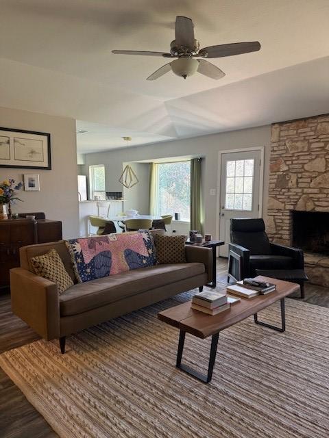 living room featuring a stone fireplace, ceiling fan, and wood finished floors