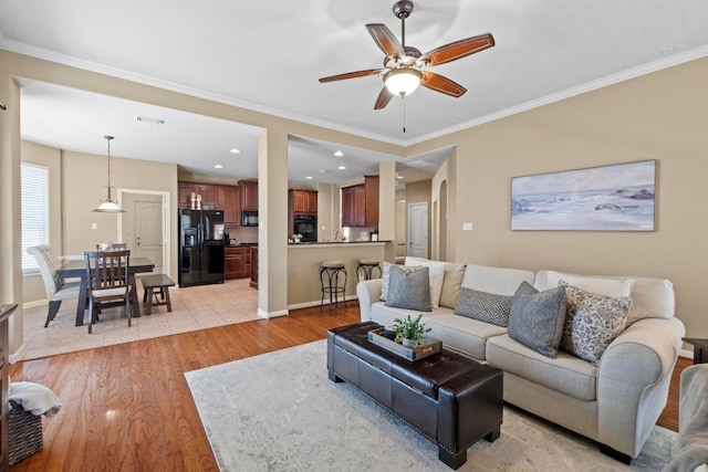 living area featuring crown molding, baseboards, and light wood finished floors