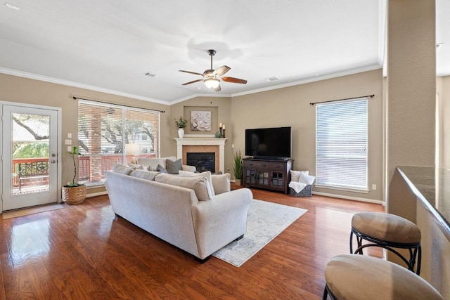 living area with a glass covered fireplace, crown molding, wood finished floors, and visible vents