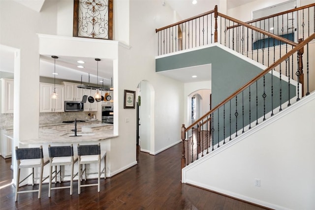 kitchen with baseboards, light stone countertops, dark wood finished floors, arched walkways, and stainless steel appliances