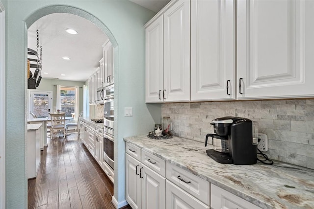 kitchen featuring white cabinets, dark wood-style floors, arched walkways, and backsplash