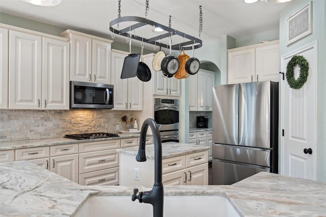 kitchen with a sink, light stone counters, tasteful backsplash, appliances with stainless steel finishes, and white cabinets