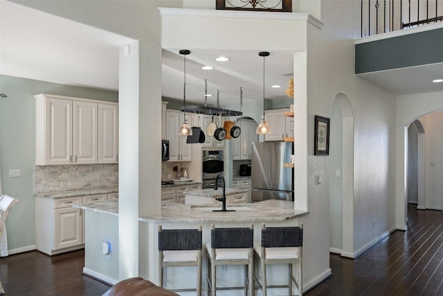 kitchen with tasteful backsplash, dark wood-style floors, appliances with stainless steel finishes, arched walkways, and a sink