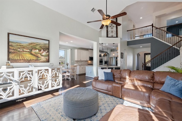 living room with visible vents, dark wood-type flooring, stairway, arched walkways, and high vaulted ceiling