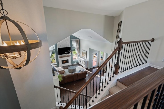 staircase with a warm lit fireplace, wood finished floors, a towering ceiling, baseboards, and ceiling fan