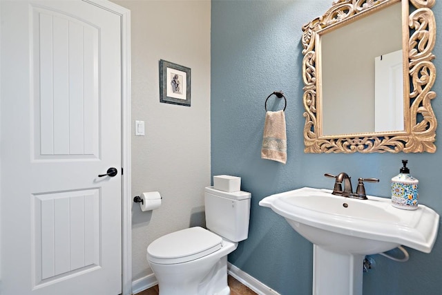 bathroom featuring toilet, baseboards, and a sink