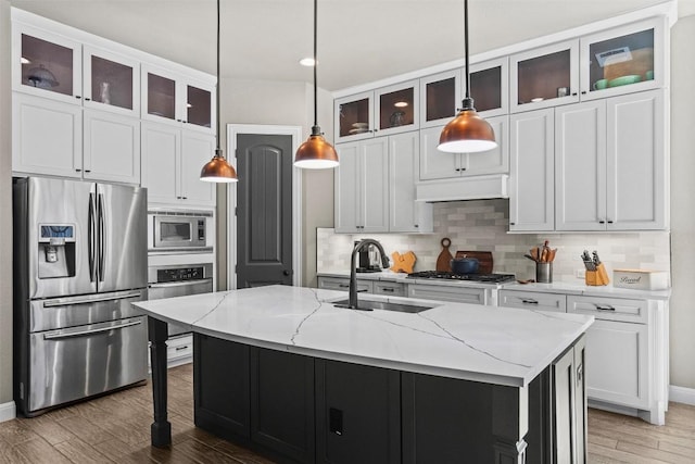 kitchen with a sink, light stone counters, backsplash, light wood-style floors, and appliances with stainless steel finishes