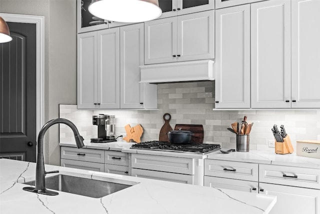 205 Varco Dr, Austin, TX 78738 - kitchen with under cabinet range hood, tasteful backsplash, glass insert cabinets, light stone counters, and white cabinetry