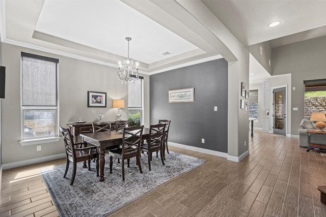 dining area with visible vents, a notable chandelier, a tray ceiling, wood finished floors, and baseboards