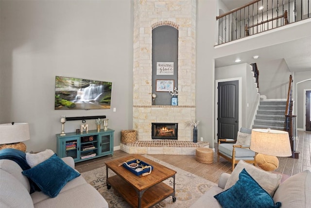 living room featuring baseboards, stairway, a stone fireplace, a high ceiling, and wood finished floors