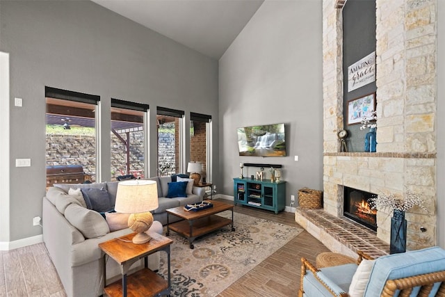 living room with baseboards, high vaulted ceiling, wood finished floors, and a fireplace