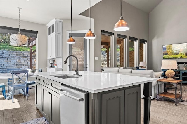 kitchen with a center island with sink, a sink, decorative light fixtures, light wood-style floors, and dishwasher