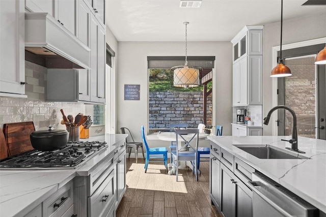 kitchen with dark wood-type flooring, a sink, appliances with stainless steel finishes, custom exhaust hood, and hanging light fixtures