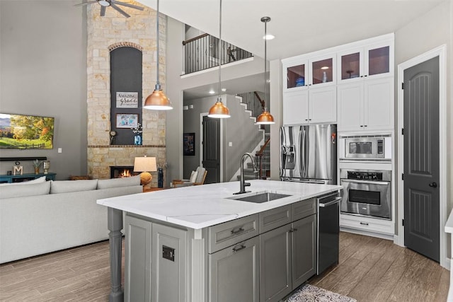 kitchen with a stone fireplace, gray cabinets, wood finished floors, stainless steel appliances, and a sink