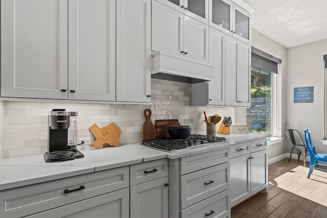 kitchen featuring backsplash, dark wood-type flooring, baseboards, premium range hood, and stainless steel gas stovetop