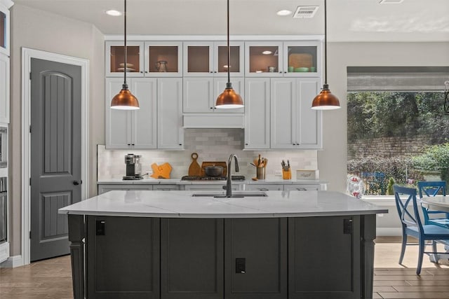 kitchen featuring visible vents, backsplash, light stone countertops, and wood finished floors