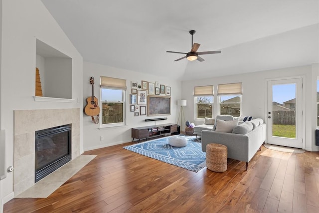 living area featuring a ceiling fan, wood finished floors, a fireplace, baseboards, and vaulted ceiling