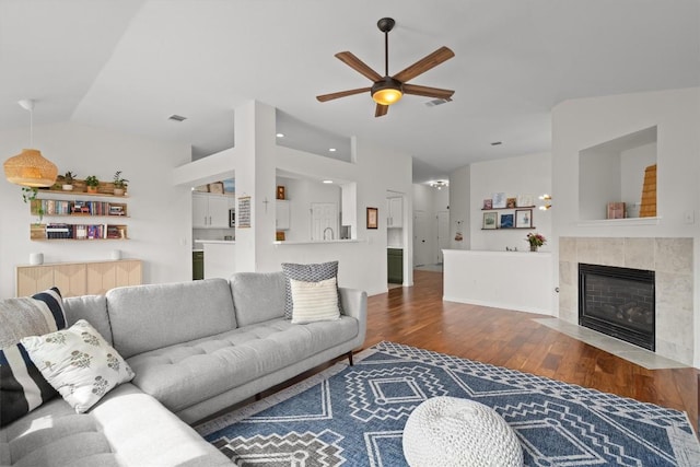 living area featuring visible vents, a ceiling fan, a tiled fireplace, wood finished floors, and vaulted ceiling