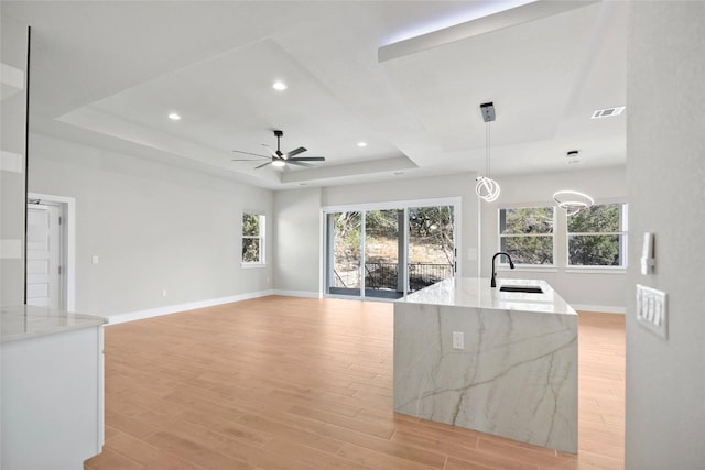 kitchen featuring baseboards, light stone counters, light wood-style flooring, a raised ceiling, and a sink