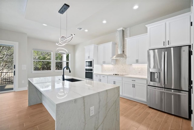 kitchen with visible vents, black electric stovetop, stainless steel fridge, wall chimney exhaust hood, and a sink