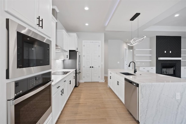 kitchen featuring light wood finished floors, ventilation hood, appliances with stainless steel finishes, white cabinetry, and a sink