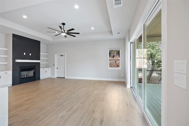 unfurnished living room featuring visible vents, a large fireplace, baseboards, light wood-type flooring, and a tray ceiling