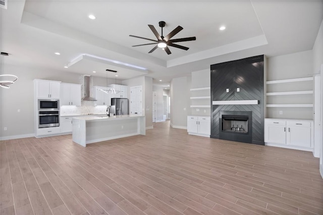 unfurnished living room featuring light wood-style floors, a large fireplace, a tray ceiling, and a sink