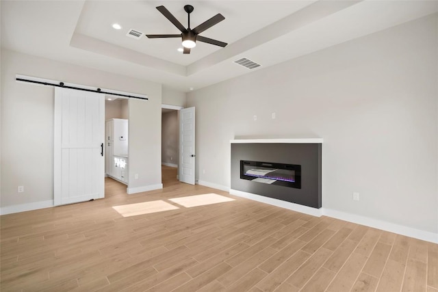 unfurnished living room featuring visible vents, light wood-type flooring, a raised ceiling, and a barn door