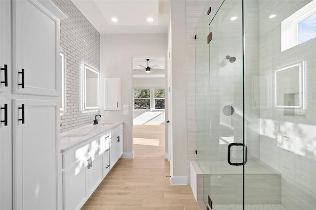 full bathroom featuring wood finish floors, a sink, backsplash, a shower stall, and double vanity