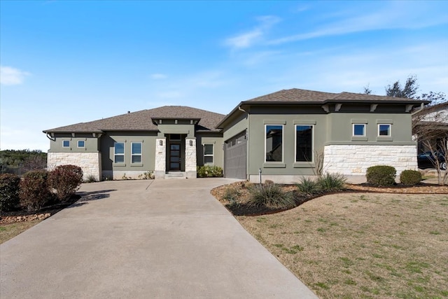 prairie-style home featuring concrete driveway, an attached garage, stone siding, and stucco siding