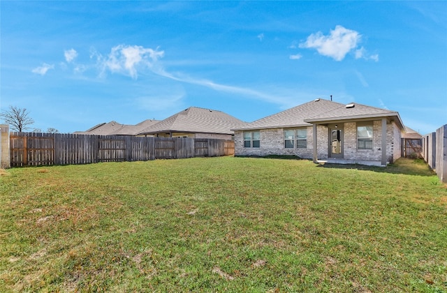 rear view of property with a yard, brick siding, and a fenced backyard