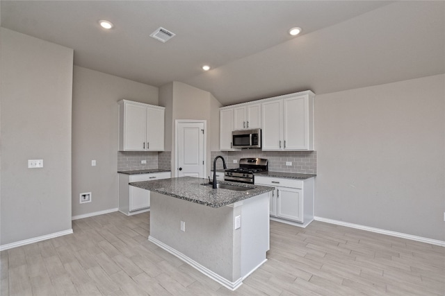 kitchen with visible vents, an island with sink, a sink, appliances with stainless steel finishes, and backsplash