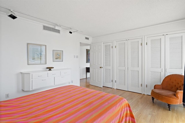 bedroom with light wood-type flooring, visible vents, multiple closets, and a textured ceiling