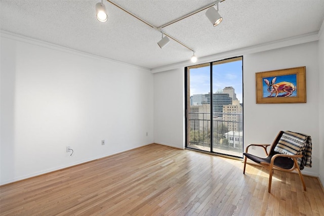 sitting room featuring track lighting, expansive windows, light wood-style flooring, a view of city, and a textured ceiling