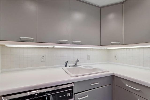 kitchen featuring a sink, dishwashing machine, decorative backsplash, and gray cabinets