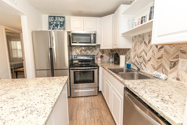 kitchen with decorative backsplash, stainless steel appliances, light wood-style floors, white cabinetry, and a sink