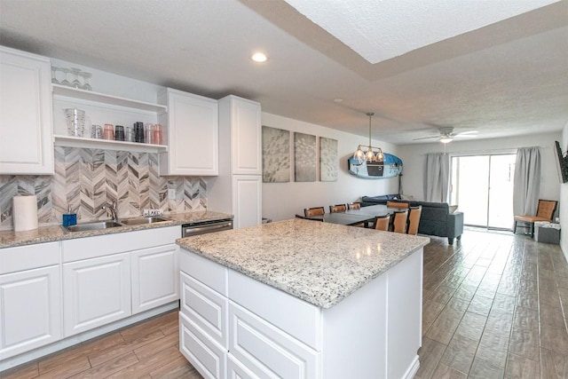 kitchen featuring light wood-style flooring, a sink, backsplash, a center island, and white cabinetry