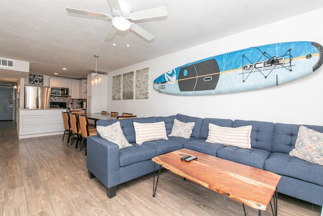 living room with visible vents, a textured ceiling, light wood-type flooring, and a ceiling fan