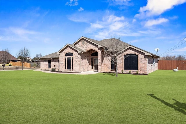 view of front of property with brick siding, a shingled roof, a front yard, and fence