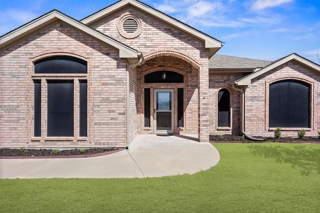 property entrance with a lawn, roof with shingles, and brick siding