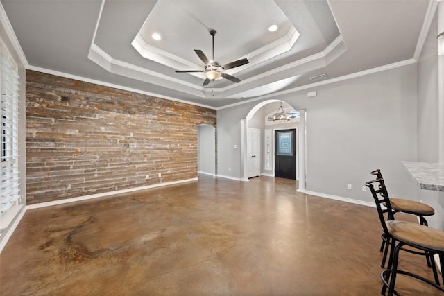 interior space with a tray ceiling, finished concrete floors, arched walkways, baseboards, and ceiling fan