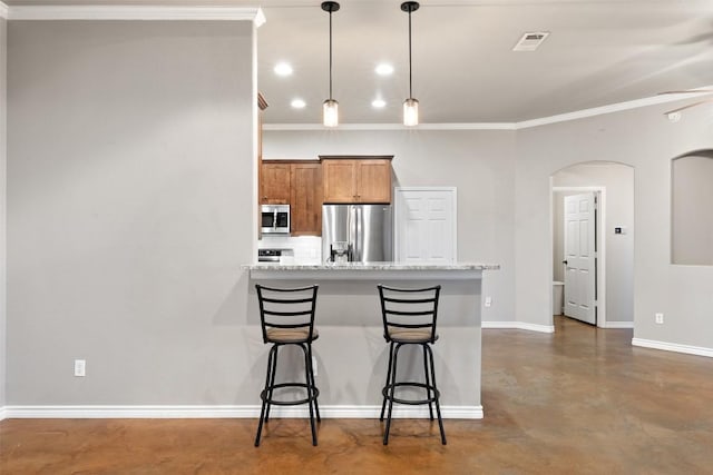 kitchen featuring visible vents, stainless steel appliances, concrete flooring, a kitchen breakfast bar, and brown cabinets