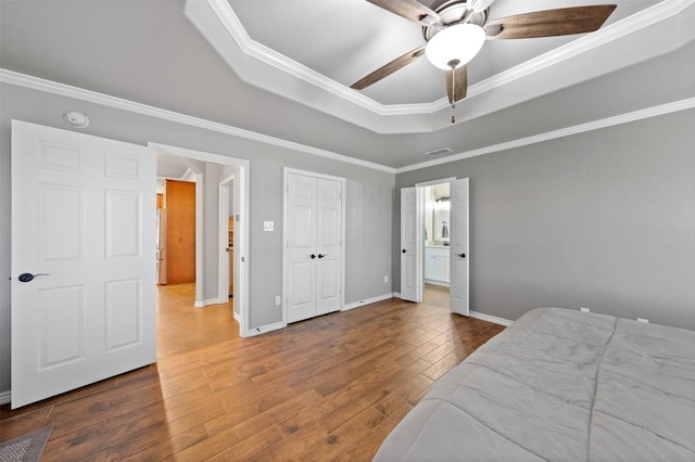 bedroom featuring ornamental molding, a tray ceiling, hardwood / wood-style floors, baseboards, and ceiling fan