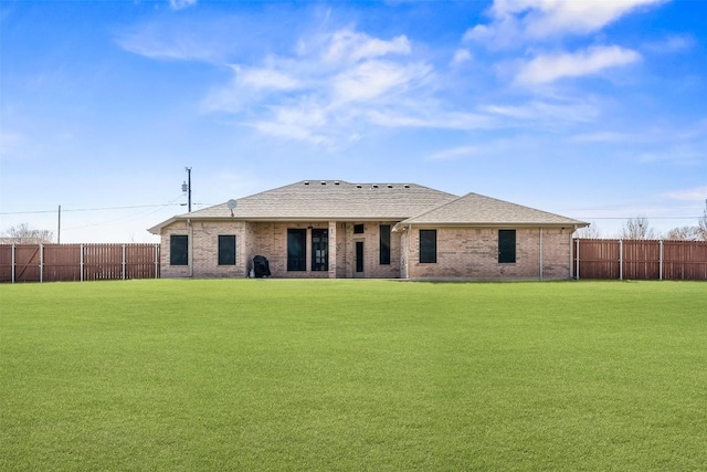 rear view of property featuring a lawn, roof with shingles, brick siding, and fence