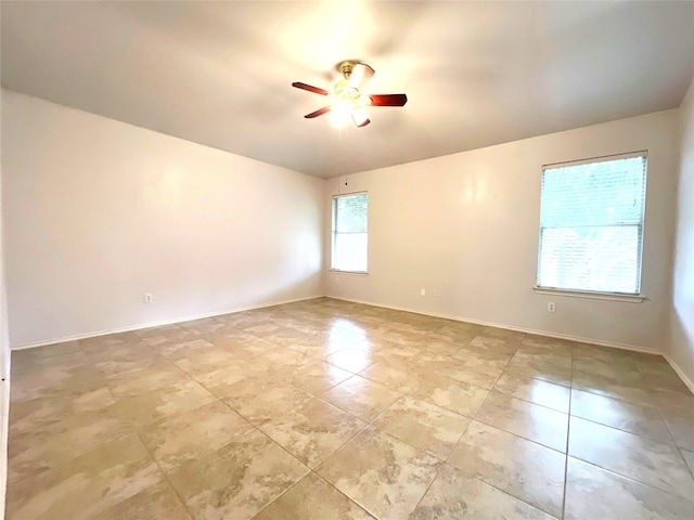 empty room featuring light tile patterned flooring, a ceiling fan, and baseboards