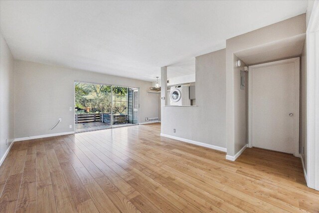 unfurnished living room featuring light wood finished floors, visible vents, stacked washer and clothes dryer, and baseboards